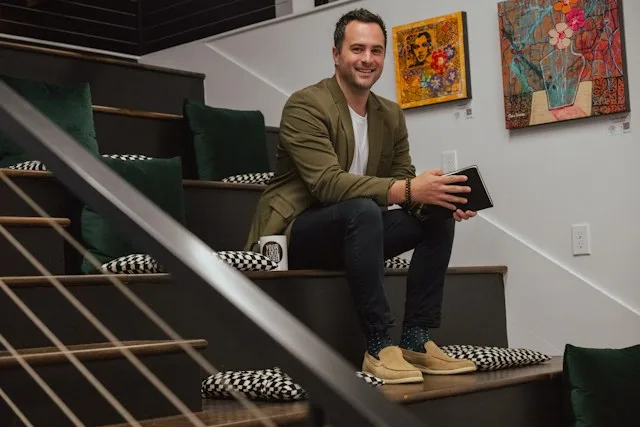 Smiling sole trader sitting on a staircase with a tablet in his hand