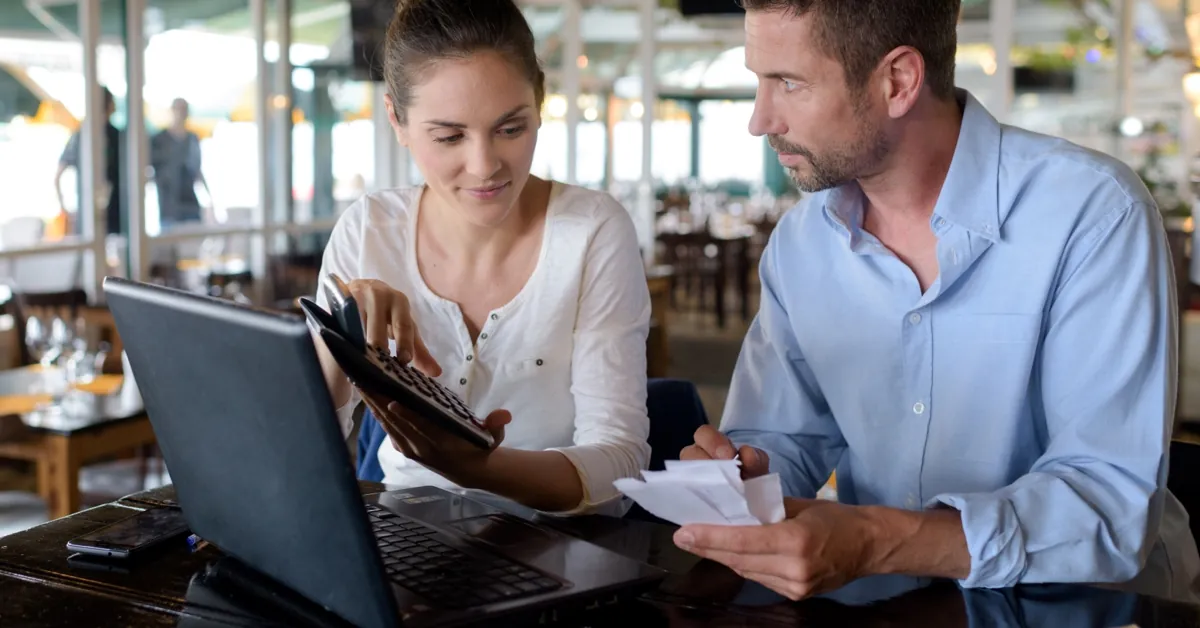 Dos personas revisando albaranes y facturas de proveedor con un portátil en el propio local